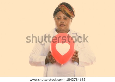 Studio shot of woman doctor holding red balloon with heart sign against chest