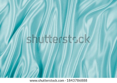 Photography of beautiful wavy turquoise silk satin luxury cloth fabric, abstract background design.