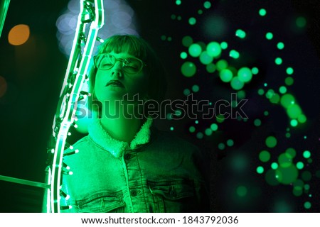 Young woman with closed eyes on dark backgrond of green neon lights and spots. Soft focus