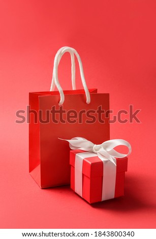 Red paper bag and gift box with bow on red background with copy space. Holiday sale concept.
