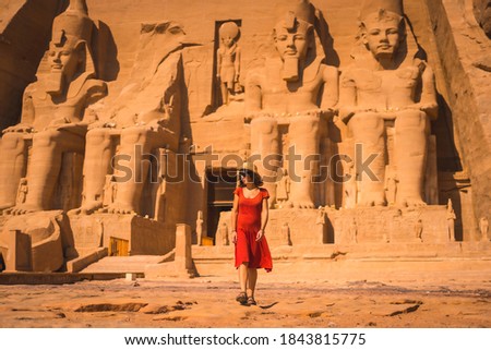 A young tourist in a red dress leaving the Abu Simbel Temple in southern Egypt in Nubia next to Lake Nasser. Temple of Pharaoh Ramses II Royalty-Free Stock Photo #1843815775