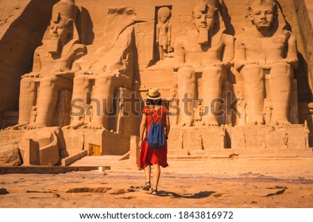 A young tourist in red dress walking towards the Abu Simbel Temple in southern Egypt in Nubia next to Lake Nasser. Temple of Pharaoh Ramses II Royalty-Free Stock Photo #1843816972