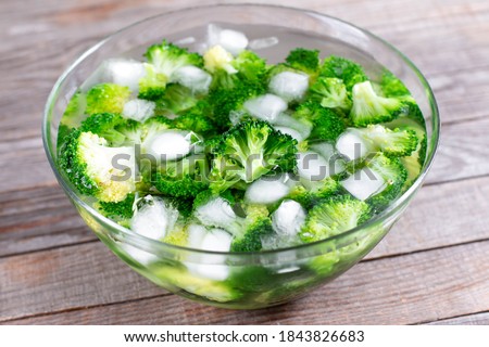 Blanched broccoli cabbage cooling down in icy water in a bowl on wooden table Royalty-Free Stock Photo #1843826683