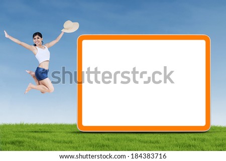 A young woman jumping next to empty board on the green grass