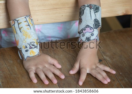 Child hands presenting a DIY activity: Homemade Animal bracelets for kids, made of used toilet paper rolls, featuring Cartoon characters of a cat and a cow.