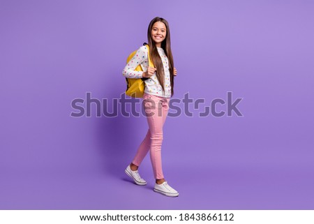 Full length body size photo of preteen girl with long hair carrying yellow backpack smiling happily isolated on bright violet background