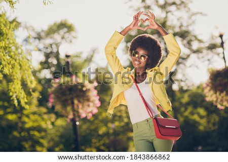 Photo portrait of attractive woman making heart with fingers holding over head in park