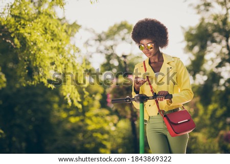 Photo portrait of hipster girl driving kick-scooter checking phone holding in one hand in park