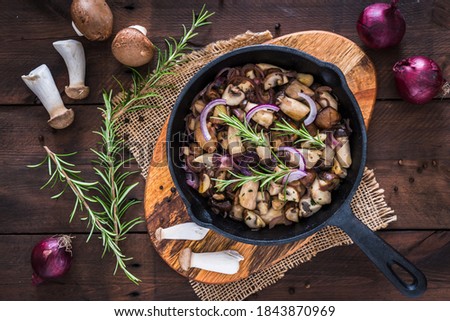 Vegetarian mushroom pan with red onions and rosemary on wooden table. Vertical photo in stock.