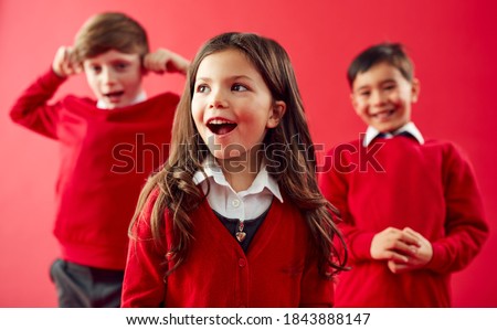 Group Of Excited Elementary School Pupils Wearing Uniform Having Fun Against Red Studio Background Royalty-Free Stock Photo #1843888147