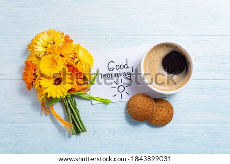 Notes good morning and coffee mug with bouquet of yellow flowers calendula on blue background. Breakfast, morning coffee, card concept, top view