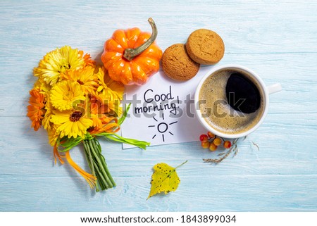 Notes good morning and coffee mug with bouquet of yellow flowers calendula and pumpkin autumn decorations on blue background. Breakfast, morning coffee, card concept, top view