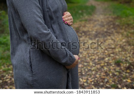 Close up picture of pregnant belly bump in third trimester outdoor in the park at fall