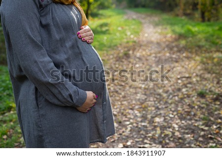 Close up picture of pregnant belly bump in third trimester outdoor in the park at fall