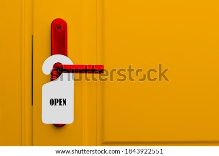 The door with the sign is open. Yellow door of hotel, restaurant or bar with red handle and paper warning label