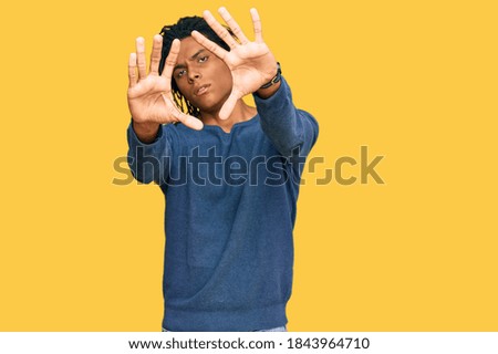 Young african american man wearing casual winter sweater doing frame using hands palms and fingers, camera perspective 