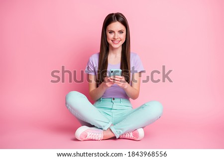 Full size photo of positive cheerful girl sit floor legs crossed use cellphone enjoy social network communication wear teal purple pants isolated over pastel color background