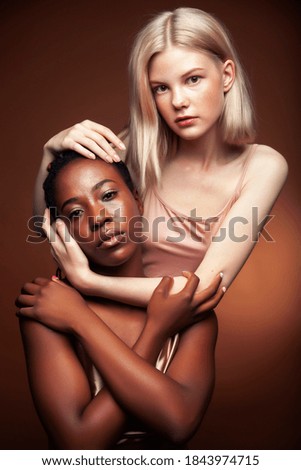 two pretty girls african and caucasian blond posing cheerful together on brown background, ethnicity diverse lifestyle people concept