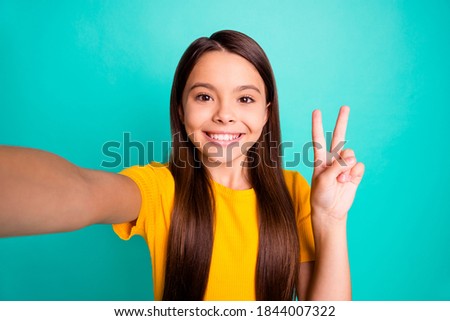 Photo of positive kid girl take selfie make v-sign wear yellow t-shirt isolated over turquoise color background