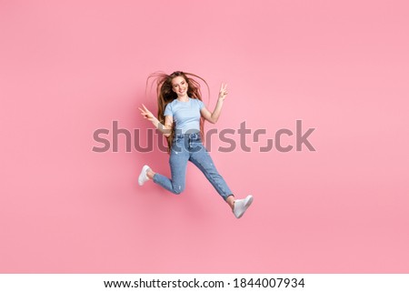 Photo portrait of girl showing two v-signs jumping up isolated on pastel pink colored background