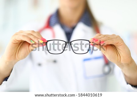 Ophthalmologist with stethoscope around neck holds glasses for vision in clinic closeup. Professional selection and sale of glasses concept.