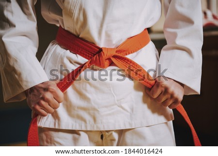 A man ties a red belt on a white kimono and pulls at the side gap. The fighter holds his belt and tightens it on the belt to start the fight. Royalty-Free Stock Photo #1844016424