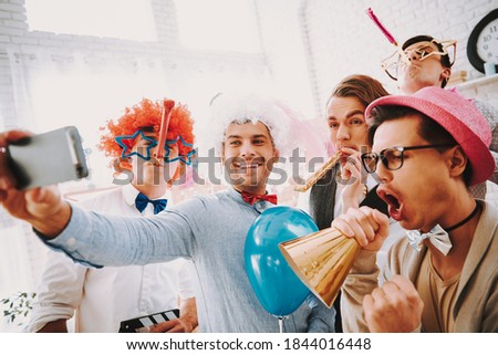 Gay guys in bow ties taking selfie on phone at party. Man in a wig stands in a room with friends and takes a photo in memory of a gay party.  Royalty-Free Stock Photo #1844016448
