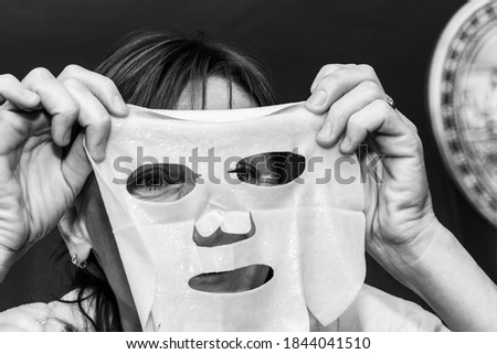 a young woman puts a white moisturizing mask on her face, black and white photo