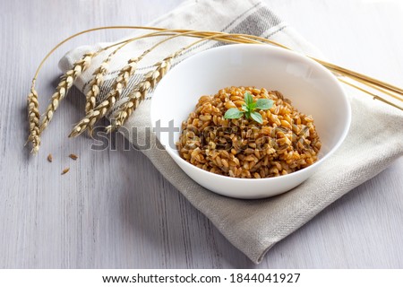 Spelt porridge in a bowl with basil leaves on linen napkin with ears of spelt grain. White wooden background. Healthy breakfast. Royalty-Free Stock Photo #1844041927