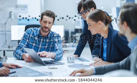 Factory Meeting Room: Multi-Ethnic and Diverse Team of Engineers, Managers, Investors Talking Sitting at Conference Table, Analyzing Blueprints, Mechanism Component. High-Tech Manufactory Optimization Royalty-Free Stock Photo #1844044246