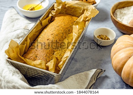 Homemade pumpkin cake with honey, poppy seeds, dried fruits, baked nuts and parchment paper, close-up. Healthy and delicious sugar-free cake recipe, next to baking ingredients. Homemade baking concept