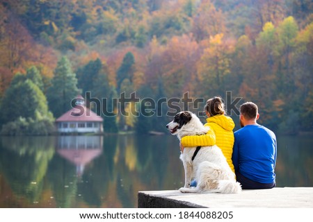 Couple with dog sitting on dock at the lake in magic autumn sun.