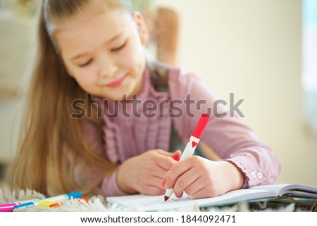 Child holds red pen in hand for painting