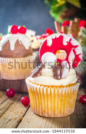 Funny Christmas cupcakes. Homemade sweet cupcakes with sugar glaze in form on christmas decoration and symbols, on wooden background with xmas decor