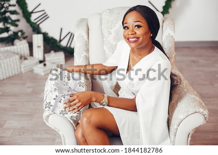 Beautiful girl in a decorated room. Woman near Christmas tree. Black lady in a white dress