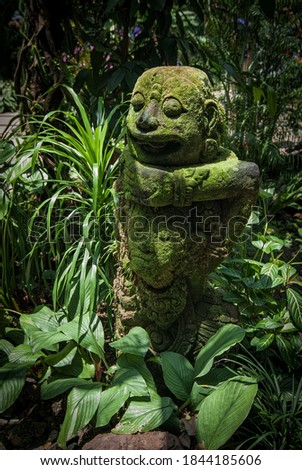 Ancient overgrown demon statue hidden in tropical garden Royalty-Free Stock Photo #1844185606