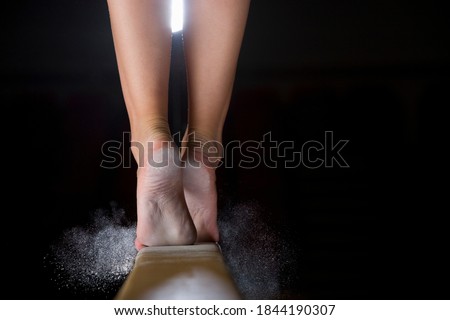 Close-up low section of a female gymnast on balance beam against a black background.