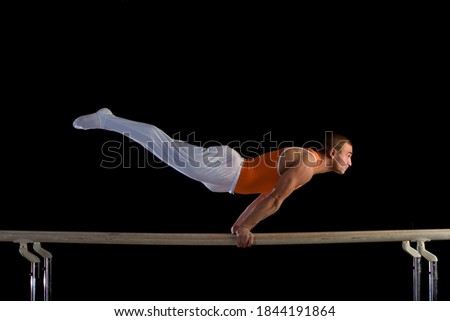 Side view of a male gymnast performing on parallel bars isolated on black background.