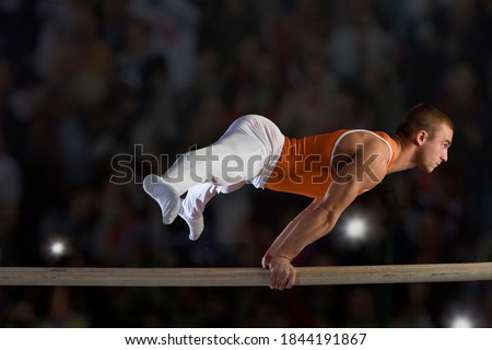 Side view of a male gymnast performing on parallel bars.