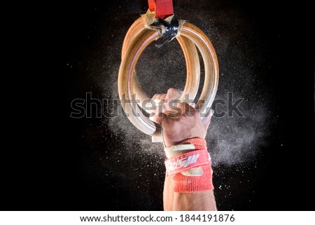 Detailed shot of male gymnast catching gymnastic rings with chalk dust on black background. Royalty-Free Stock Photo #1844191876