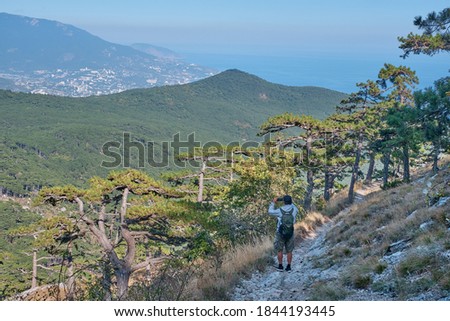 Beautiful landscape of the southern Crimea. Scenic slope of Ai Petri mountain. A man with a backpack is walking along the rocky mountain trail and taking a pictures by a smartphone.