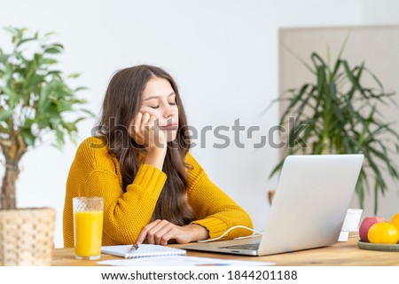 Young girl fell asleep in front of laptop. Cute woman is bored, tired or overworked. Cozy home environment. Pretty female in bright yellow jumper working on laptop at home
