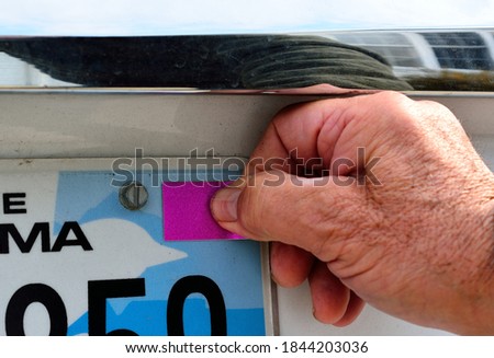 Selective focus on thumb pressing the blank annual license registration on rear license plate with copy or text space. The Man's righthand is pressing the blank violet sticker on the license plate. 