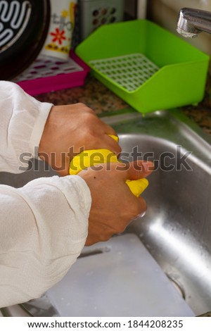 Woman cleaning the sink with a yellow cloth.