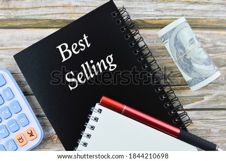 Top view of calculator, banknote, pen, and notebooks with writing text 'Best Selling' on wooden background. Business concept.