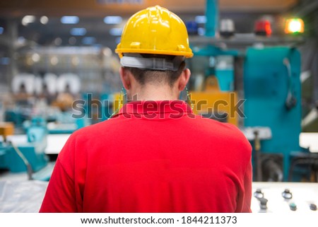 Factory worker in red t-shirt and yellow helmet works on control panel Royalty-Free Stock Photo #1844211373
