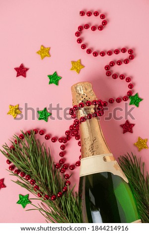 Champagne bottle with beads garland, pine needles and stars on pink background. Object for new year, Christmas and holiday compositions