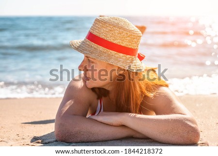 Tanning young girl in a hat and swimsuit lies on the beach. Summer holiday fashion concept