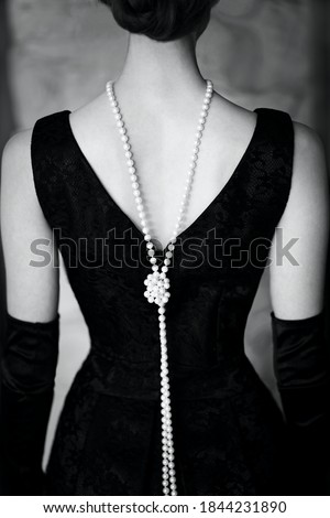 Beautiful female figure from the back in a black dress and pearls in the style of 20-30 years of the 20th century. Black and white photo Royalty-Free Stock Photo #1844231890