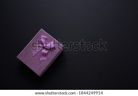 Single festive violet gift box with small shiny bow. Black background. Metallised box cover. Wrapping gifts.
